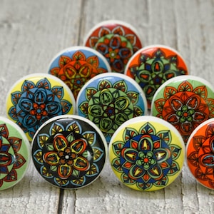 May include: A set of ten ceramic cabinet knobs featuring colourful mandala designs. The knobs are round and have a white base with a variety of colours, including red, orange, yellow, green, blue, and black.