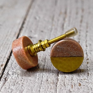 May include: Two round cabinet knobs with a pink marble top and a gold metal bottom. The knobs have a brass screw.