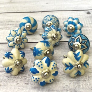 Könnte beinhalten: Zehn blaue und weiße Keramik-Schubladengriffe mit silbernen Akzenten. Die Griffe zeigen verschiedene florale und geometrische Muster.