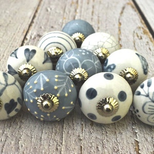 Könnte beinhalten: Eine Sammlung von 12 Keramik-Schubladengriffen in verschiedenen blauen und weißen Blumenmustern. Die Griffe haben eine goldfarbene Metallbasis.