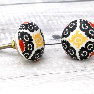 Könnte beinhalten: Zwei Keramik-Knöpfe mit einem schwarz-weißen Muster. Die Knöpfe haben eine silberne Schraube und einen roten Akzent.