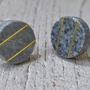 May include: Two round grey marble cabinet knobs with gold accents. The knobs have a textured surface and are accented with two thin gold lines.
