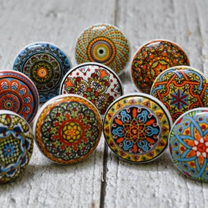 May include: Assortment of ten ceramic cabinet knobs with colourful, intricate mandala designs. The knobs are round and have a white base with a variety of colours including blue, red, yellow, orange, and green.