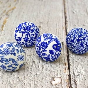 Könnte beinhalten: Vier blaue und weiße Keramikknöpfe mit Blumenmustern. Die Knöpfe sind rund und haben eine glänzende Oberfläche.
