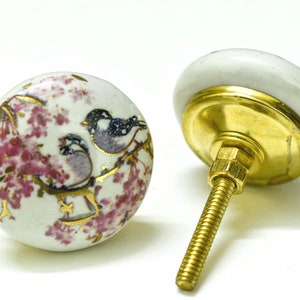 May include: White ceramic knob with a gold screw and a floral design featuring two birds and pink flowers.