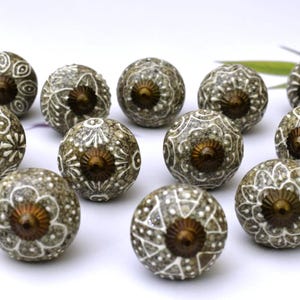 May include: A set of 12 ceramic cabinet knobs with a gray and white floral design. The knobs have a brass finish and are perfect for adding a touch of elegance to any room.