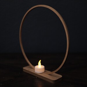 May include: A wooden ring with a small candle on a wooden base. The ring is made of natural wood and has a simple design. The candle is a small, white tea light.