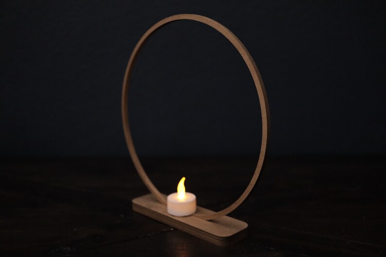 May include: A wooden ring with a small candle on a wooden base. The ring is made of natural wood and has a simple design. The candle is a small, white tea light.