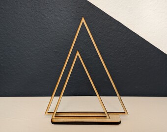 May include: A wooden geometric triangle stand with two layers. The stand is made of natural wood and has a simple, modern design.