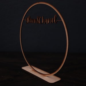 May include: A wooden hoop with the text "Glenn & Chanel" written on it. The hoop is standing on a wooden base.
