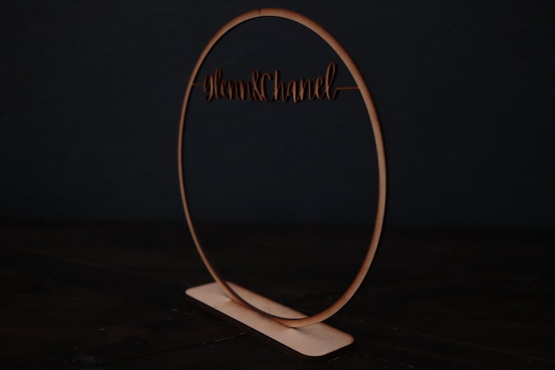 May include: A wooden hoop with the text "Glenn & Chanel" written on it. The hoop is standing on a wooden base.