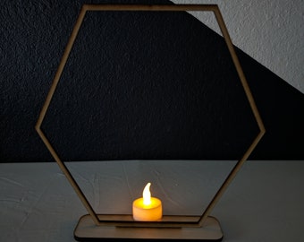 May include: A wooden hexagonal frame with a small, lit candle in the center. The frame is on a white surface.