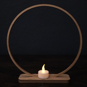 May include: A wooden ring with a small, white candle in the center. The ring is on a wooden base and the candle is lit.