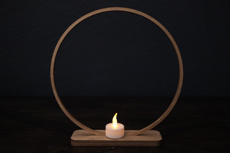 May include: A wooden ring with a small, white candle in the center. The ring is on a wooden base and the candle is lit.