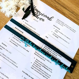 Könnte beinhalten: Nahaufnahme einer Strickanleitung mit dem Text "Honeycomb Haven SOCKS". Zwei schwarze und teal Stricknadellehren liegen auf der Anleitung. Der Text "Ruhe bewahren und weiter stricken" ist in Teal.