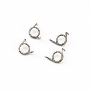 Op de afbeelding: Vier zilveren metalen veerclips, elk met een kleine lus en een gebogen uiteinde. De clips zijn in een vierkant op een witte achtergrond gerangschikt.