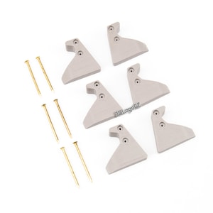 May include: Six grey plastic corner brackets with six gold tacks. The brackets have a textured surface and are designed to be used for mounting shelves or other objects.