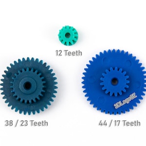 May include: Three plastic gears in shades of blue and teal are displayed against a white background. The gears vary in size, with the smallest gear having 12 teeth. The other two gears have 38/23 and 44/17 teeth, respectively. The text "3DLogoGZ" is visible on one of the gears.