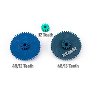Könnte beinhalten: Drei Zahnräder aus Kunststoff in Blau- und Grüntönen vor weißem Hintergrund. Die großen Zahnräder haben 48 Zähne, die kleinen 12 und 13. Text zeigt die Zähnezahl.