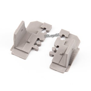 Może przedstawiać: Dwa szare, drukowane w 3D elementy układanki o zazębiających się kształtach. Każdy element ma konstrukcję kątową z prostokątną podstawą i pionową sekcją. Na elementach widoczny jest tekst "3DLogoGZ". Elementy znajdują się na białym tle.