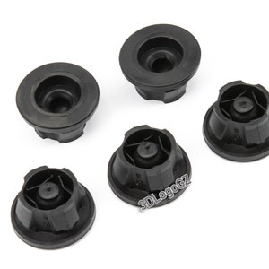 Puede incluir: Cinco tapones para patas de muebles de plástico negro con superficie texturizada. Los tapones tienen una base circular y un centro elevado con un pequeño agujero.