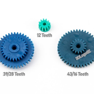 Op de afbeelding: Drie plastic tandwielen, een blauwe met 39/28 tanden, een blauwe met 43/16 tanden en een groene met 12 tanden.