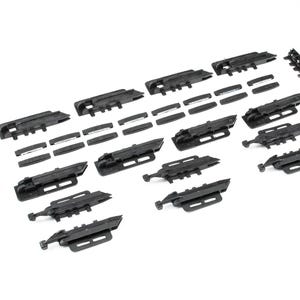 Puede incluir: Un surtido de componentes de plástico negro, que incluyen varias piezas rectangulares e inserciones rectangulares más pequeñas. Las piezas están dispuestas sobre una superficie blanca, lo que sugiere un kit o un conjunto de artículos relacionados. Los componentes parecen nuevos y sin usar.