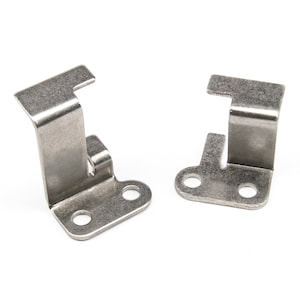 Może przedstawiać: Dwa metalowe wsporniki ze stali nierdzewnej. Każdy wspornik ma zagiętą, prostokątną górną część, pionowe podparcie i podstawę z dwoma okrągłymi otworami. Przeznaczone do montażu lub mocowania przedmiotów.