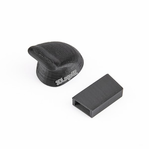 May include: Two black 3D printed objects. One is a curved, rounded shape, and the other is a rectangular block with a rectangular hole in the centre.