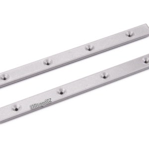 Pode incluir: Duas tiras de metal prateadas, retangulares com bordas arredondadas, cada uma com cinco orif&iacute;cios embutidos espa&ccedil;ados uniformemente. As tiras est&atilde;o dispostas diagonalmente sobre um fundo branco. O texto "3DLogoGZ" &eacute; vis&iacute;vel em uma tira.