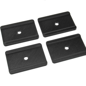 May include: Four black plastic spacers with a hole in the center. The spacers are rectangular and have a textured surface.