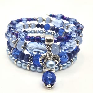 Könnte beinhalten: Ein mehrreihiges Armband mit blauen und silbernen Perlen, verziert mit einem silbernen Anhänger mit einem blauen Edelstein. Das Armband besteht aus verschiedenen Blautönen, darunter hellblau, dunkelblau und silber.