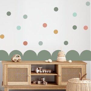 May include: A wooden cabinet with woven doors and a collection of wooden toys. The wall behind the cabinet is white with colourful polka dots and a green scalloped border. Toys include a car, train, stacking rings, and alphabet blocks.