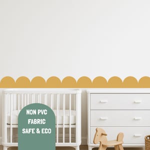 May include: Mustard yellow scalloped wall decal above a white cot and chest of drawers. The decal is made of non-PVC fabric and is safe and eco-friendly. The nursery furniture includes a white cot and a white chest of drawers.
