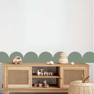 May include: A light wood cabinet with woven door fronts, displaying wooden toys. A wooden car, a train, and a stacking ring toy are visible. The cabinet is set against a white wall with a green scalloped border.