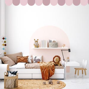 May include: A child's bedroom scene featuring a white bed with cushions and a brown blanket. A plush lion and bear are on the bed. A small desk and chair are to the right. A woven rug and basket are in the foreground. The room has a pink accent wall.