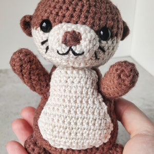May include: A brown and white crocheted otter soft toy with black eyes and a stitched smile.
