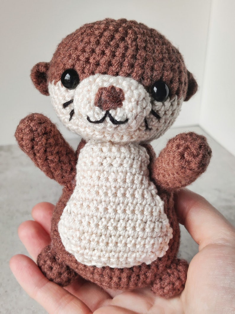 May include: A brown and white crocheted otter soft toy with black eyes and a stitched smile.