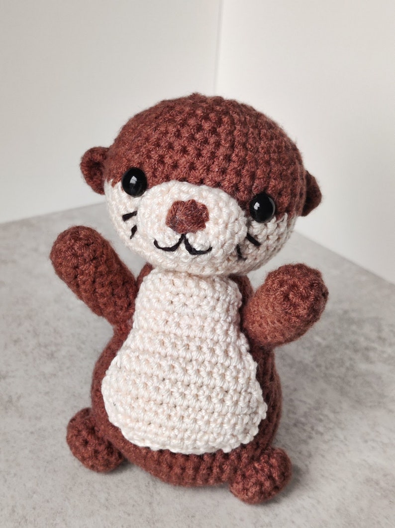 May include: A brown and white crocheted otter plush toy with black eyes and a smiling face.
