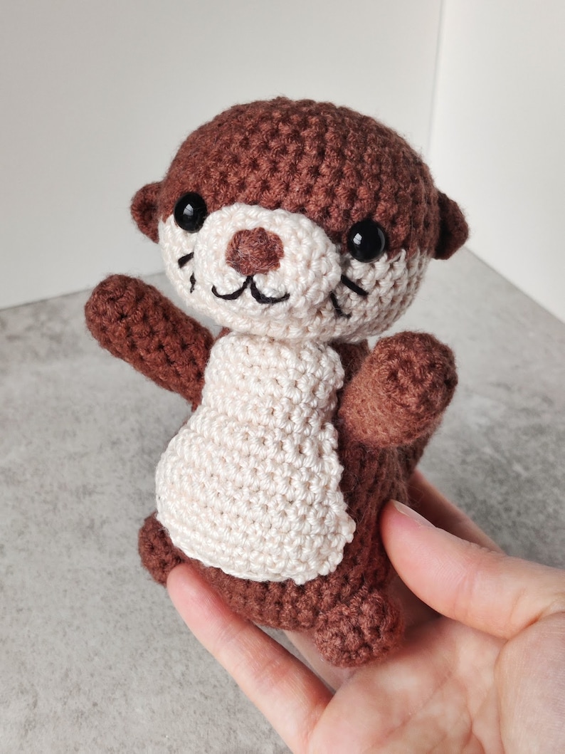 May include: A brown and white crocheted otter plush toy with black eyes and a smiling mouth.