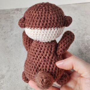 May include: A brown crocheted otter soft toy with a white crocheted tummy.