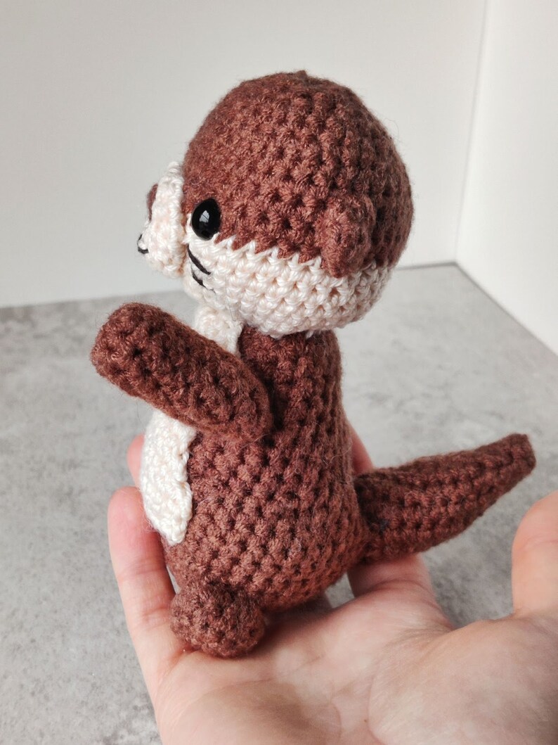 May include: A brown and white crocheted otter toy with black eyes. The otter is standing on its hind legs with its tail curled behind it.