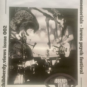 Pode incluir: Fotografia a preto e branco de duas pessoas a atuar num palco. A pessoa à esquerda canta num microfone e a pessoa à direita toca guitarra. A fotografia é do número 002 de "Chibberdy Views" dos memoriais do "Lewes Psych Festival".