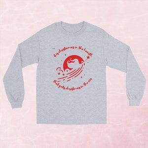 Könnte beinhalten: Graues Langarmshirt mit einer roten Grafik einer Fee mit einem Stern und dem Text "Es ist Weihnachten im Herzen, das Weihnachten in die Luft bringt."