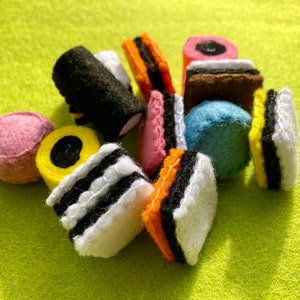 May include: A collection of felt licorice sweets in various colours and patterns, including black and white, yellow and black, pink, and blue.