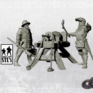 Puede incluir: Un modelo 3D impreso de un trebuchet medieval con dos figuras, una con armadura y otra con ropa civil. El trebuchet está hecho de madera y cuerda, y las figuras están posadas como si estuvieran operando la máquina. El modelo está impreso en plástico gris y tiene una escala de aproximadamente 28 mm a 34 mm.