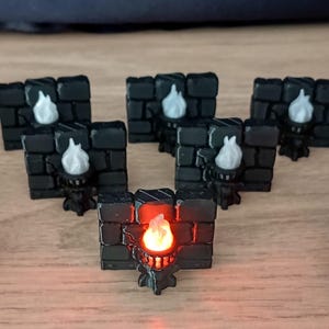 Pode incluir: Seis seções de parede de tijolo preto em miniatura com uma pequena tocha no centro de cada uma. Cinco das tochas têm chamas brancas e uma tem uma chama vermelha.
