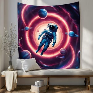 Op de afbeelding: Een wandkleed met een astronaut die in een draaiende nevel zweeft met planeten en sterren. De astronaut draagt een wit ruimtepak met een rood vizier. De nevel is een levendige mix van roze, paars en blauw.