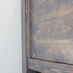May include: Close-up of a dark brown wooden headboard with a simple design. The headboard is made of planks of wood that are joined together to create a rustic look.
