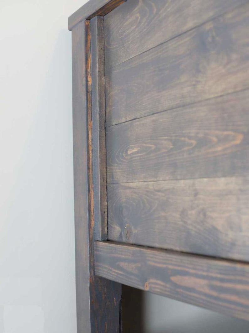 May include: Close-up of a dark brown wooden headboard with a simple design. The headboard is made of planks of wood that are joined together to create a rustic look.